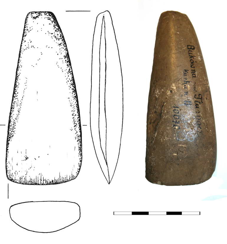 Siekierka kamienna z łupku menolitowego. Przekrój soczewkowaty, długość 10 cm, szerokość obucha 1,5 cm, ostrza – 4,5 cm, grubość 1,8 cm
